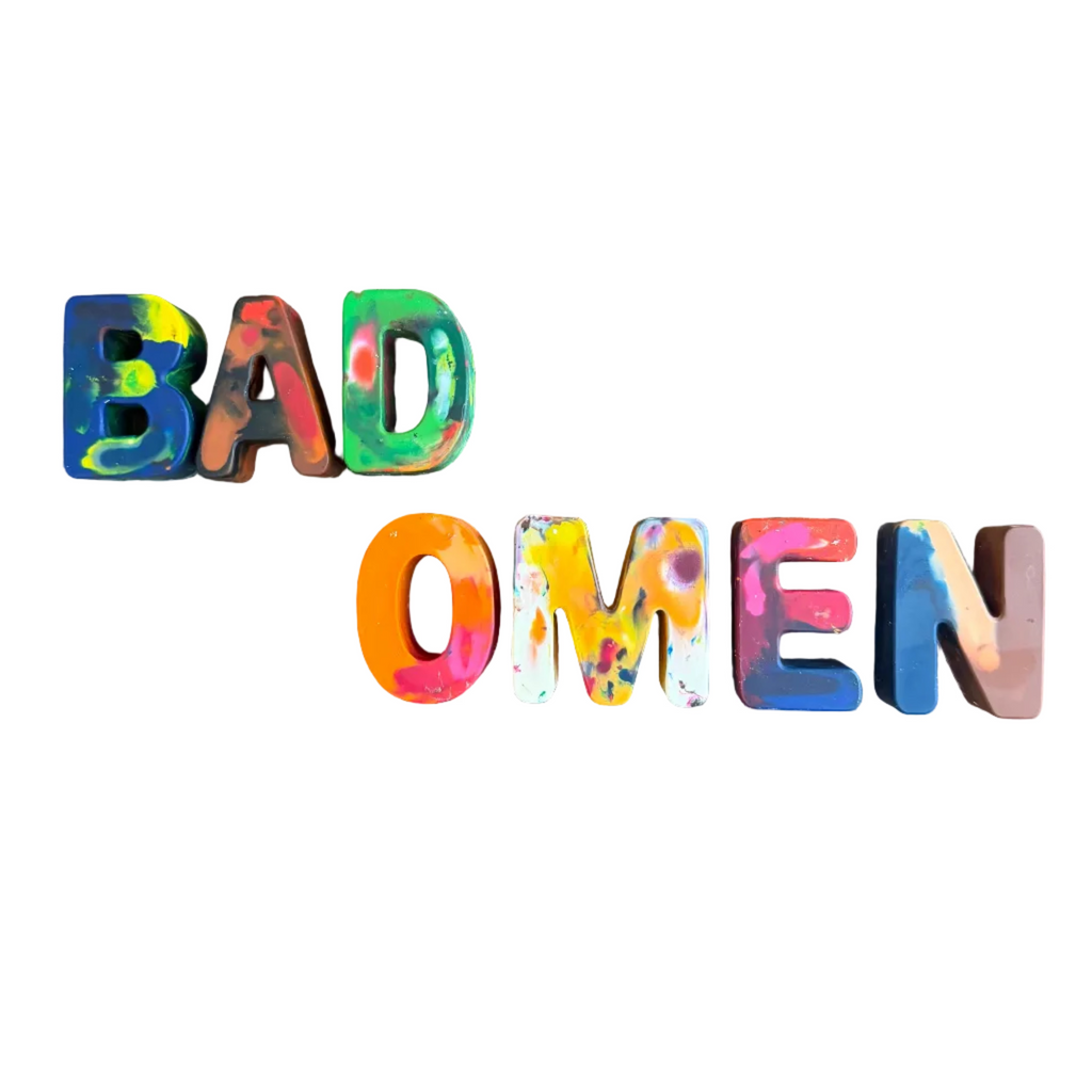 Multicolored 3D letters spelling 'BAD OMEN' arranged in two lines on a plain white background.